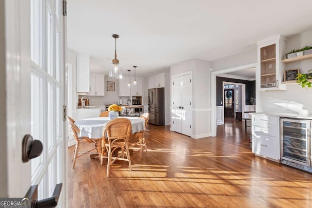 kitchen with stainless steel fridge, a kitchen breakfast bar, beverage cooler, white cabinets, and hanging light fixtures