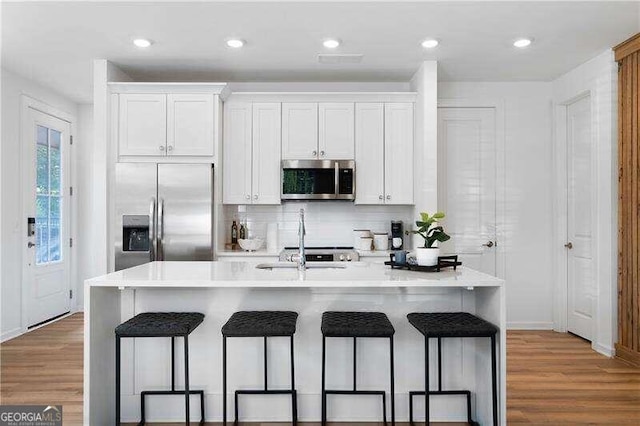 kitchen featuring a breakfast bar, white cabinetry, a center island with sink, and stainless steel appliances