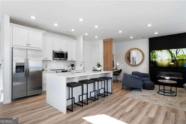 kitchen featuring stainless steel appliances, sink, white cabinetry, a breakfast bar area, and an island with sink