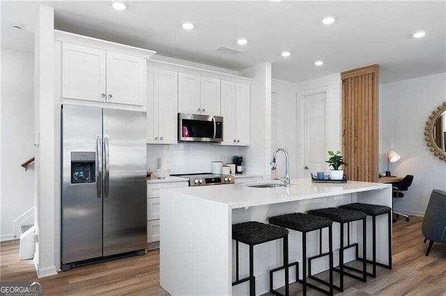 kitchen featuring sink, dark wood-type flooring, stainless steel appliances, a center island with sink, and white cabinets