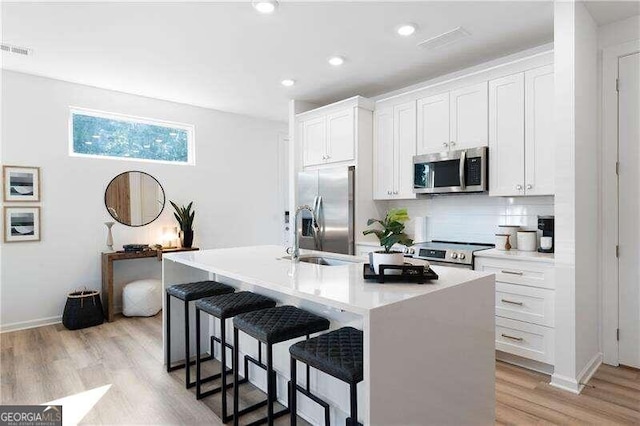 kitchen featuring a kitchen breakfast bar, white cabinetry, a center island with sink, and appliances with stainless steel finishes