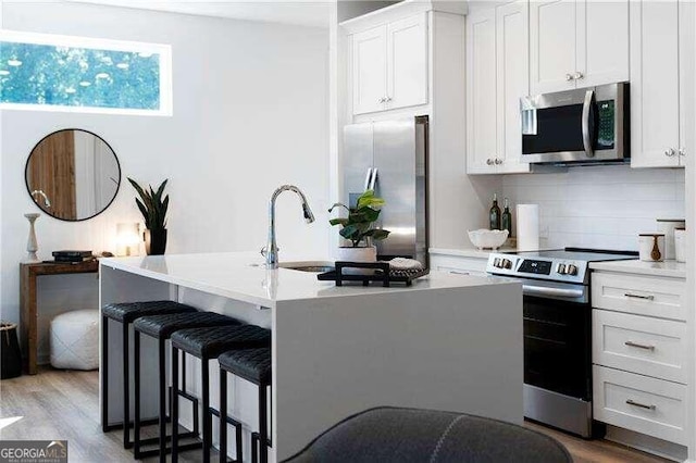 kitchen with white cabinets, a breakfast bar, stainless steel appliances, and a center island with sink