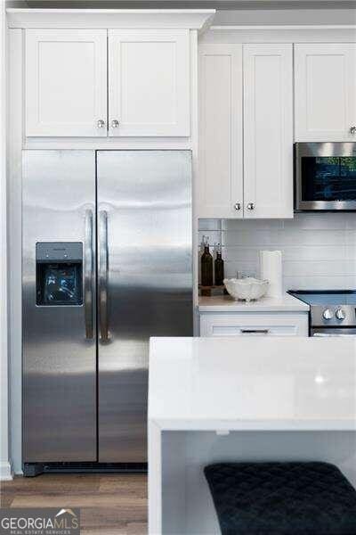 kitchen with backsplash, white cabinetry, dark wood-type flooring, and appliances with stainless steel finishes