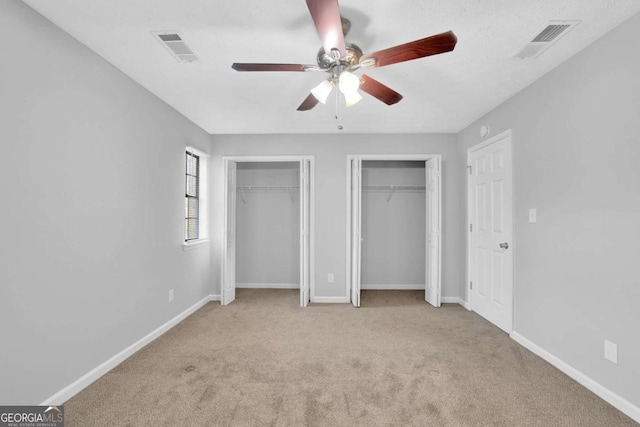 unfurnished bedroom with multiple closets, ceiling fan, and light carpet