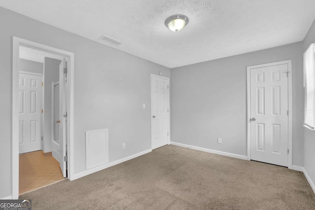 unfurnished bedroom with a textured ceiling and light colored carpet