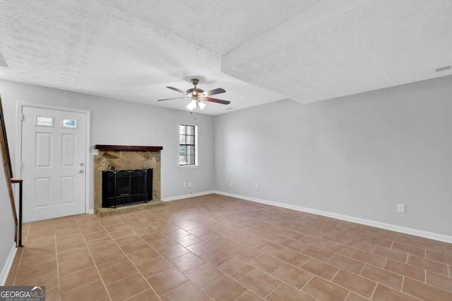 unfurnished living room with a fireplace, a textured ceiling, ceiling fan, and light tile patterned flooring