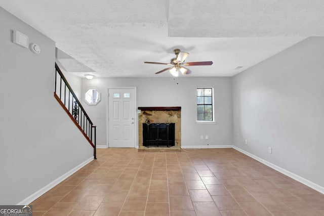 unfurnished living room with ceiling fan, a stone fireplace, light tile patterned floors, and a textured ceiling