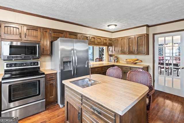 kitchen featuring sink, a textured ceiling, ornamental molding, appliances with stainless steel finishes, and hardwood / wood-style flooring