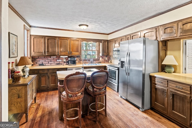 kitchen with sink, appliances with stainless steel finishes, wood-type flooring, ornamental molding, and a kitchen bar