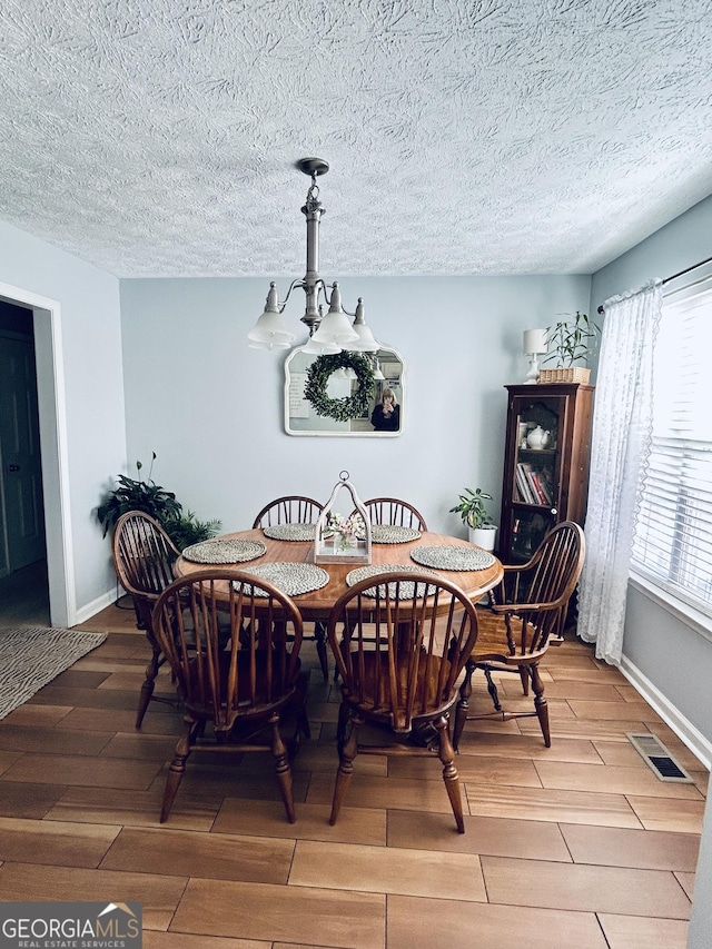 dining area featuring wood-type flooring, a textured ceiling, and an inviting chandelier