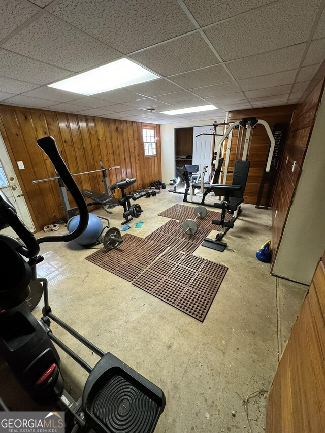 workout area with wood walls and a drop ceiling