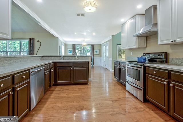 kitchen with wall chimney range hood, light wood-type flooring, dark brown cabinets, white cabinetry, and stainless steel appliances