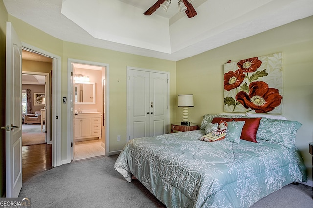 carpeted bedroom with ensuite bath, a raised ceiling, a closet, and ceiling fan