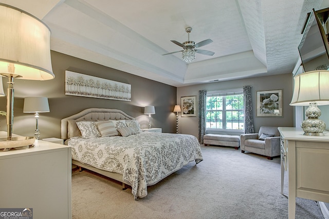 bedroom with light carpet, a textured ceiling, a raised ceiling, and ceiling fan