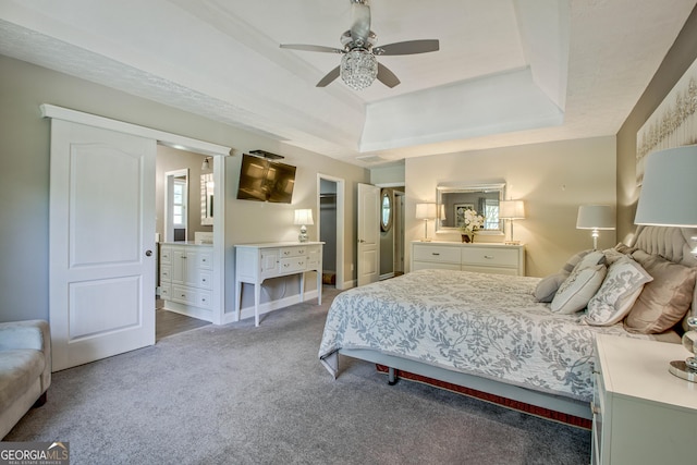 bedroom featuring a tray ceiling, ceiling fan, carpet flooring, and ensuite bathroom