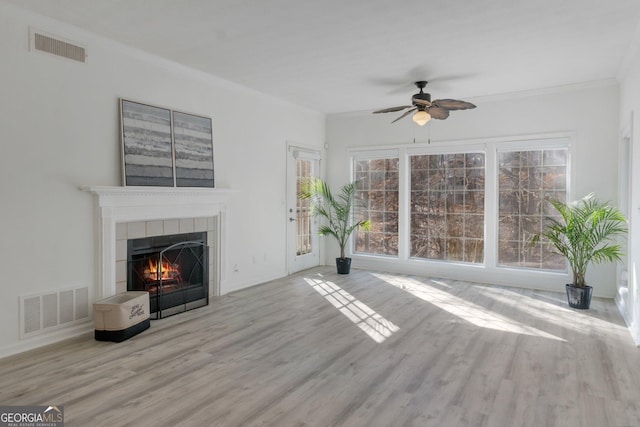 unfurnished living room with a tiled fireplace, ornamental molding, ceiling fan, and light hardwood / wood-style flooring