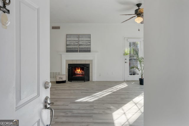 living room featuring a tiled fireplace, ceiling fan, and light hardwood / wood-style floors