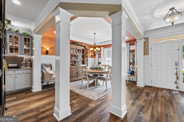 dining area with decorative columns, crown molding, dark wood-type flooring, and an inviting chandelier