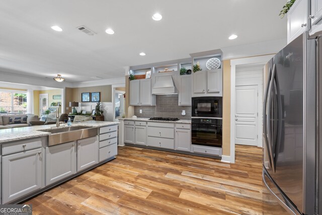 kitchen with sink, premium range hood, backsplash, light hardwood / wood-style floors, and black appliances