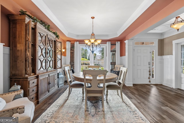 dining space with a raised ceiling, dark wood-type flooring, crown molding, and an inviting chandelier