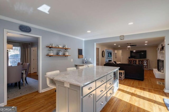 kitchen featuring ceiling fan, light stone countertops, light wood-type flooring, a kitchen island, and ornamental molding