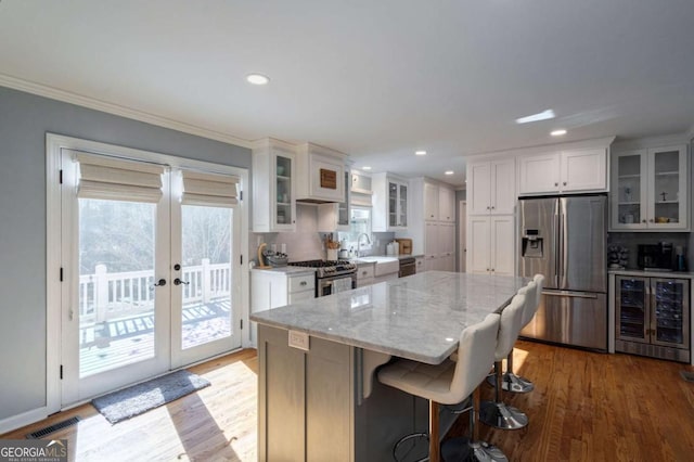 kitchen with light stone countertops, a center island, wine cooler, white cabinets, and appliances with stainless steel finishes