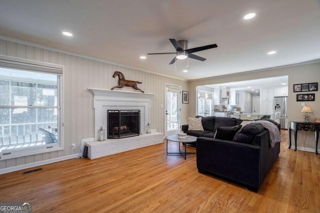 living room with a fireplace, light wood-type flooring, ceiling fan, and ornamental molding