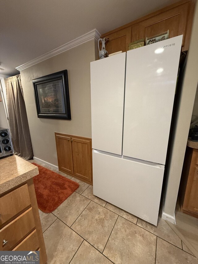 kitchen with white refrigerator, ornamental molding, and light tile patterned floors