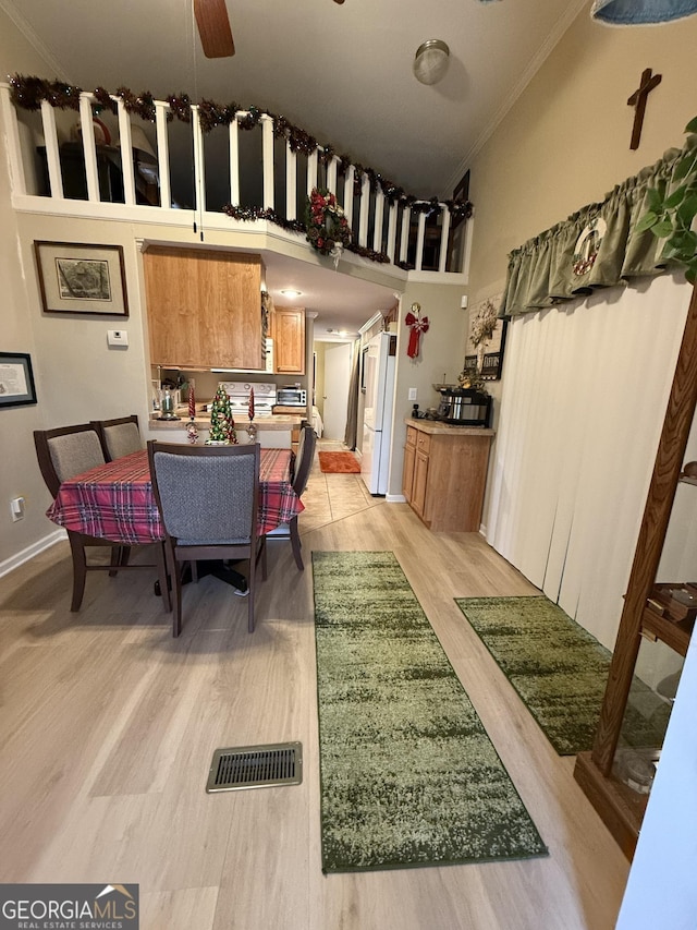 dining room featuring ceiling fan, light hardwood / wood-style floors, a high ceiling, and crown molding