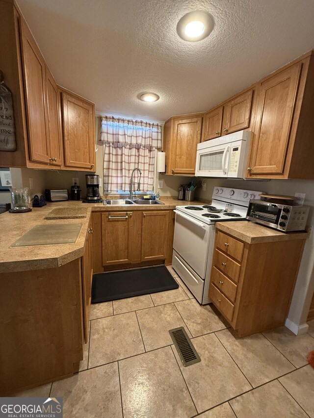 kitchen with a textured ceiling, white appliances, sink, and light tile patterned floors