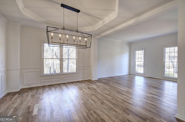 unfurnished dining area featuring ornamental molding, a tray ceiling, and wood-type flooring