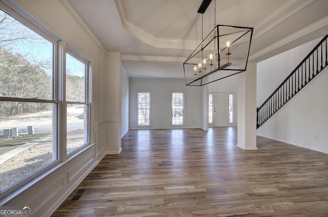 interior space with a raised ceiling, a chandelier, ornamental molding, and hardwood / wood-style flooring