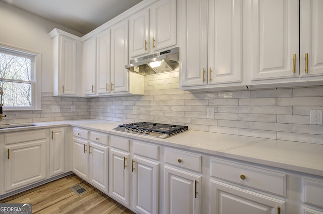 kitchen with light hardwood / wood-style floors, stainless steel gas cooktop, light stone counters, white cabinets, and sink