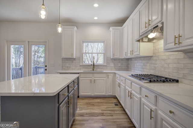 kitchen with a kitchen island, stainless steel gas cooktop, white cabinetry, and sink