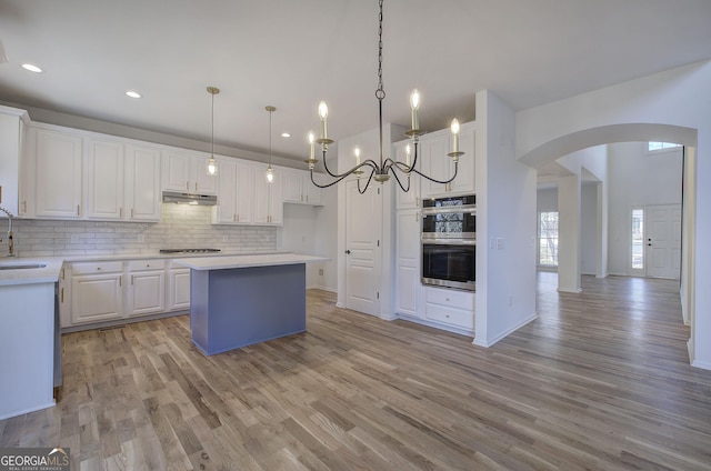 kitchen with sink, decorative light fixtures, white cabinetry, stainless steel double oven, and a kitchen island