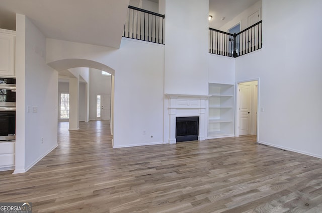 unfurnished living room featuring a high ceiling, light hardwood / wood-style floors, and built in features