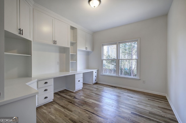 unfurnished office featuring built in desk and light hardwood / wood-style flooring