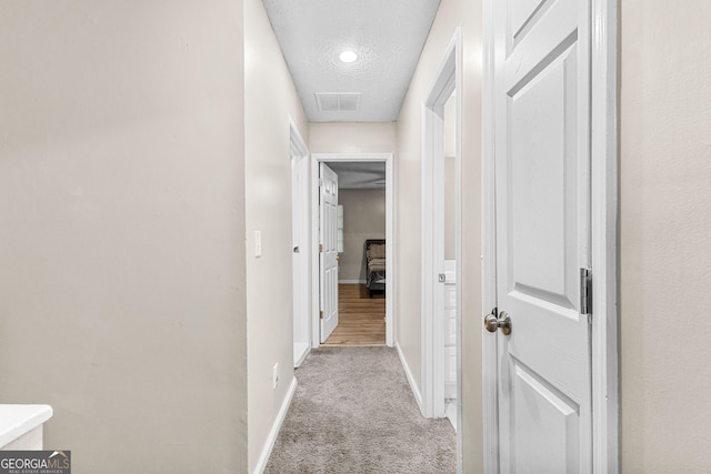 hall with light colored carpet and a textured ceiling