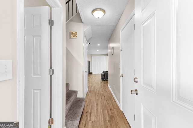 hall with light wood-type flooring and a textured ceiling