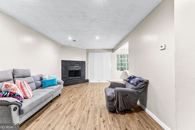 living room featuring light hardwood / wood-style floors, a stone fireplace, and a textured ceiling