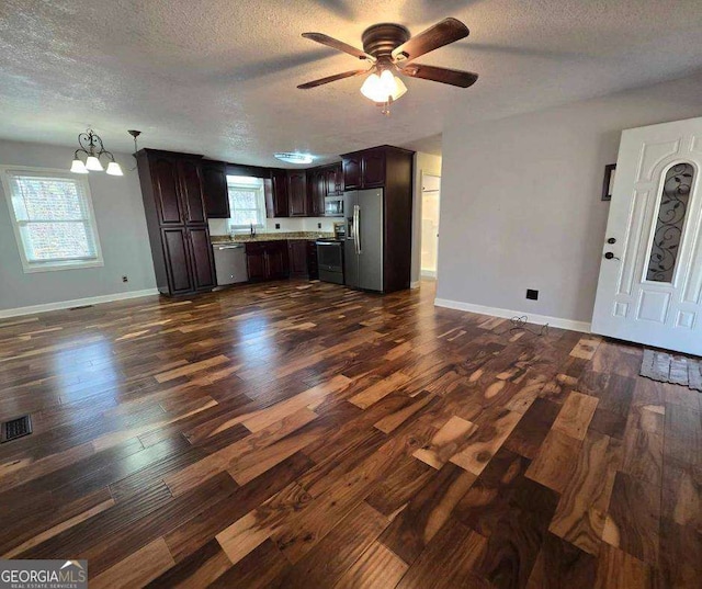 kitchen featuring dark brown cabinets, ceiling fan with notable chandelier, a textured ceiling, stainless steel appliances, and dark wood-type flooring