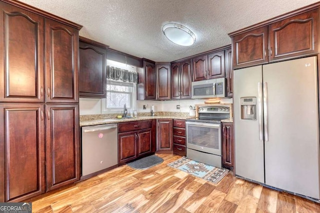 kitchen featuring light stone counters, a textured ceiling, appliances with stainless steel finishes, and light hardwood / wood-style flooring