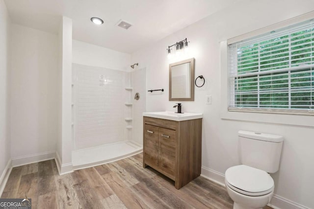 bathroom featuring tiled shower, vanity, hardwood / wood-style flooring, and toilet