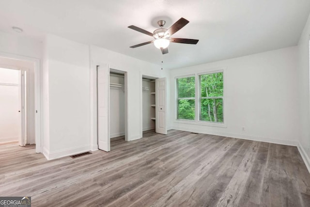 unfurnished bedroom with light wood-type flooring, ceiling fan, and multiple closets