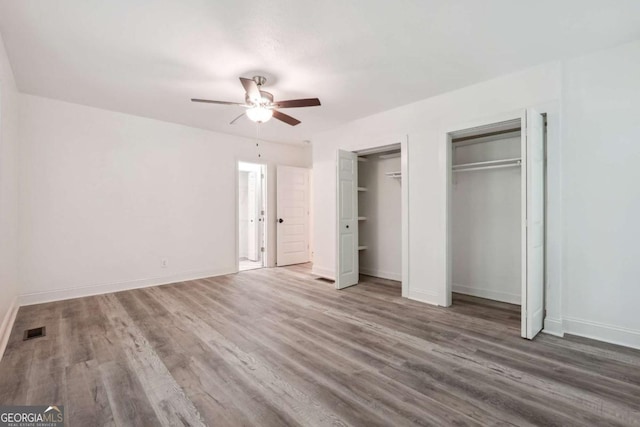 unfurnished bedroom featuring hardwood / wood-style floors, ceiling fan, and multiple closets