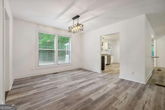 unfurnished dining area with a chandelier and light wood-type flooring