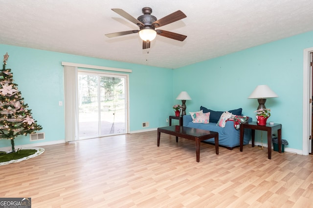 living area featuring a textured ceiling, light wood-type flooring, and ceiling fan