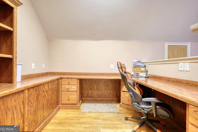 office area featuring lofted ceiling, light wood-type flooring, and built in desk