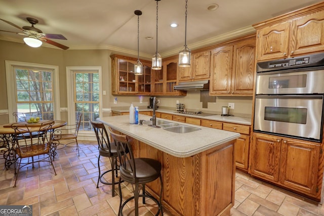 kitchen featuring ceiling fan, hanging light fixtures, double oven, a kitchen island with sink, and ornamental molding