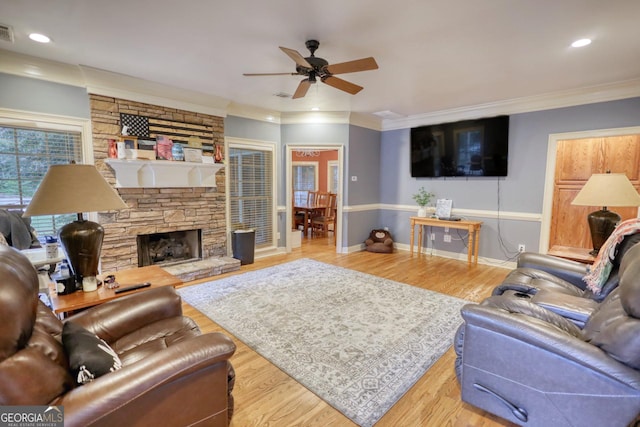 living room featuring a stone fireplace, ceiling fan, ornamental molding, and light wood-type flooring